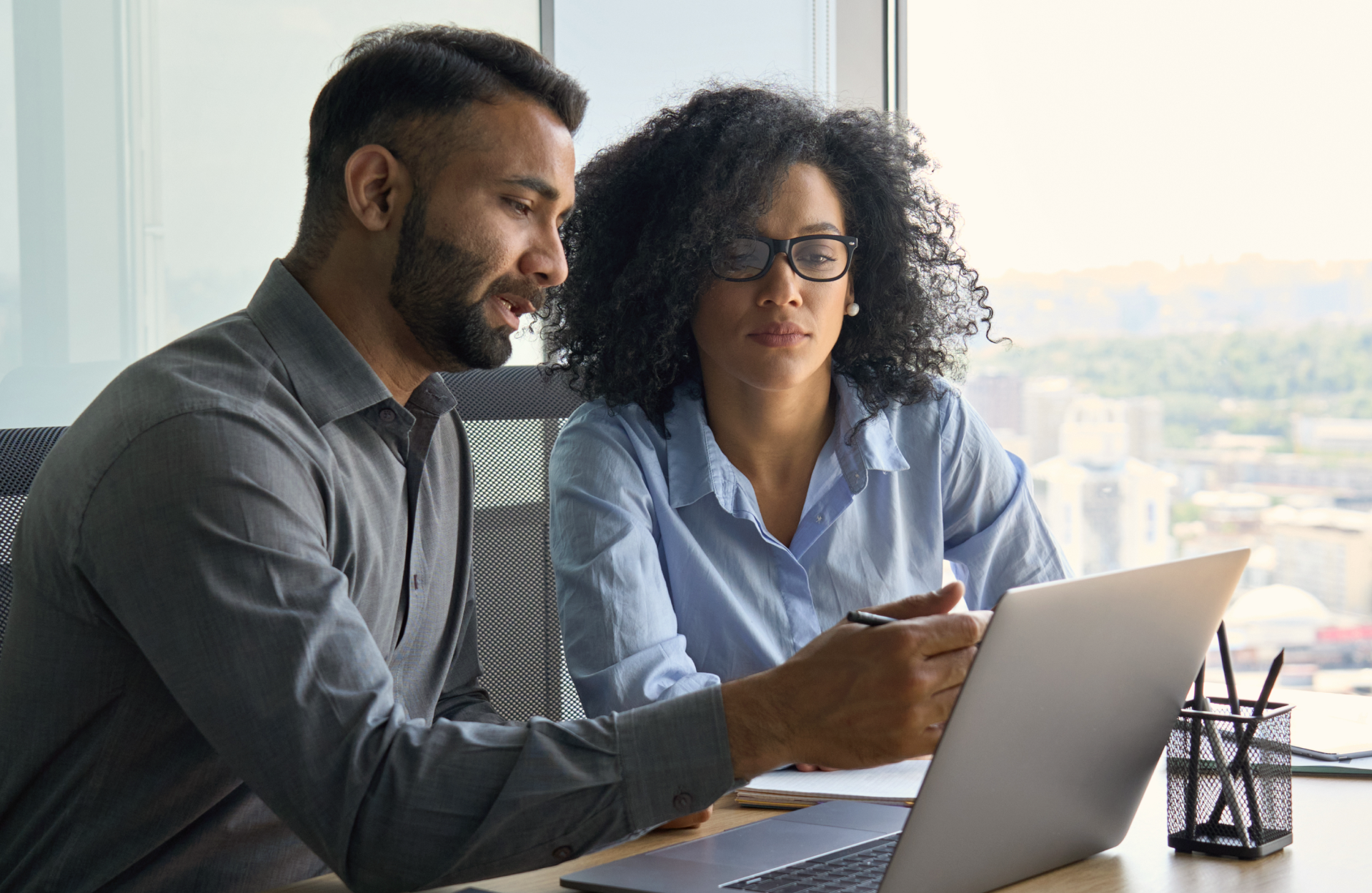 A man and woman sit in an office and review a laptop together.